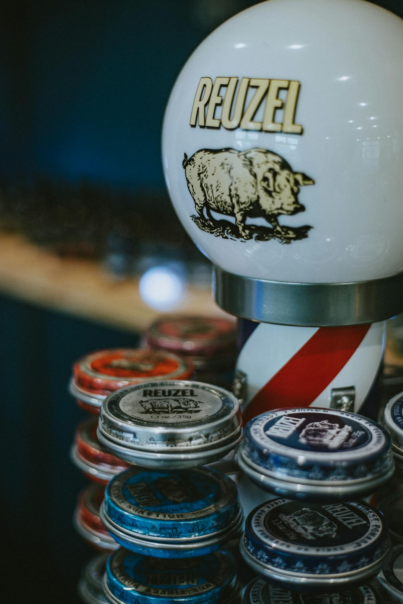 A collection of Reuzel hair products in a stylish barber shop setting with a vintage barber pole lamp.