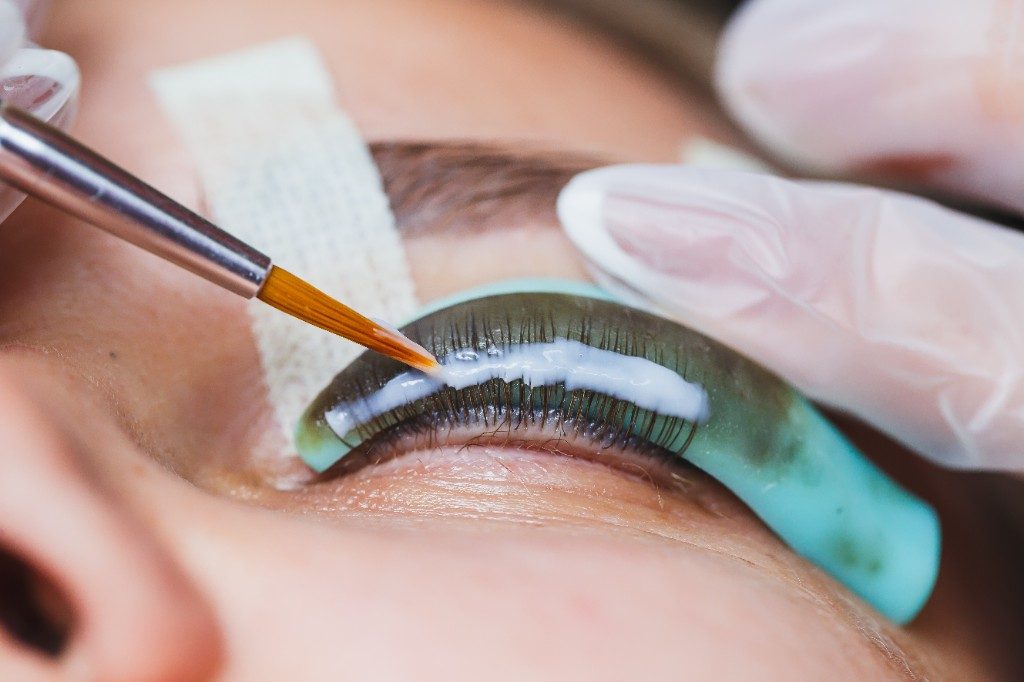 Ein Pinsel trägt das helle Lifting-Präparat auf die Wimpern auf